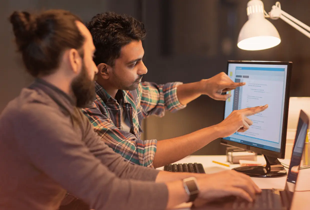 Two professionals collaborating on a desktop computer while discussing technology strategy, representing CTO outsourcing and leadership in software development.